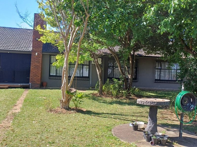 Rear view of the house featuring a brick chimney, tiled roof, security bars on windows, and a small wooden deck area.