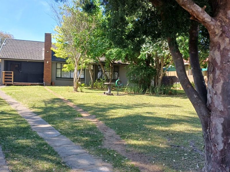Front view of a single-story house featuring a tiled roof, brick chimney, and a spacious front garden with a paved driveway.
