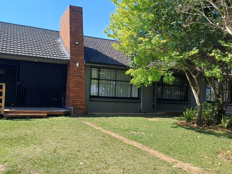 Rear view of the house featuring a brick chimney, tiled roof, security bars on windows, and a small wooden deck leading to the garden.