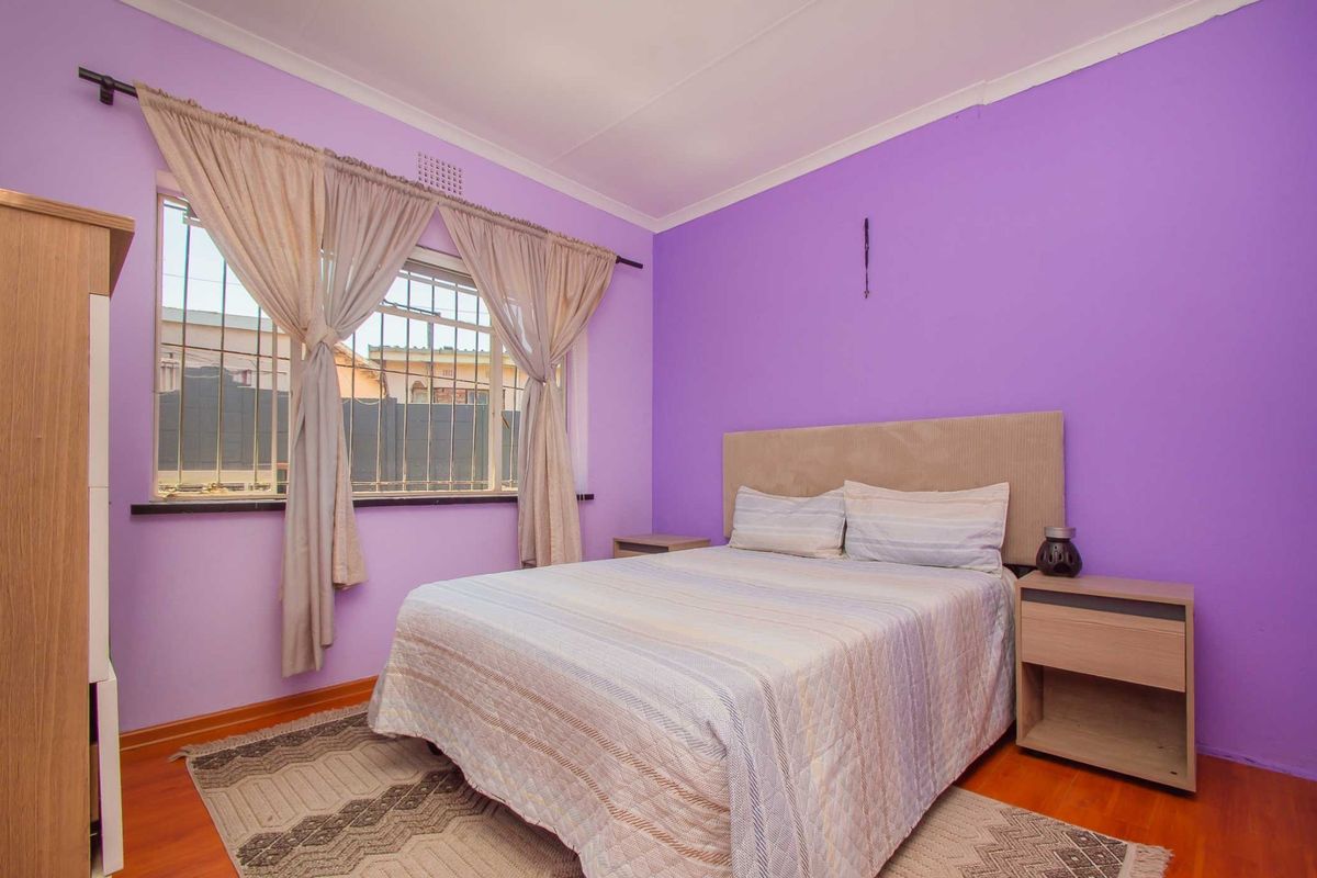A bedroom featuring laminate flooring, security bars on the window, and a neutral color palette, offering a functional and comfortable living space.