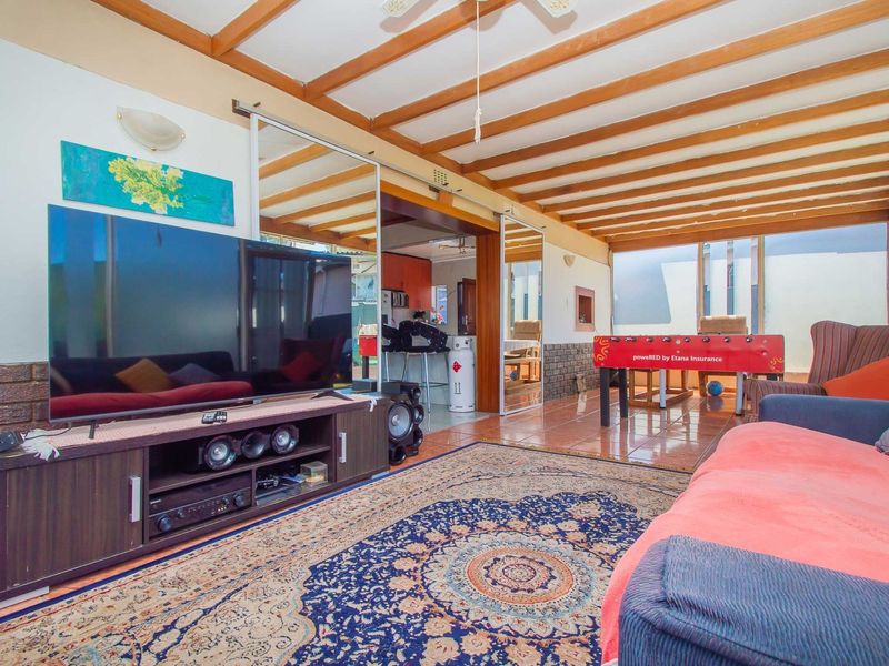Spacious living area featuring exposed timber ceiling beams, tiled flooring, and a brick feature wall, with sliding mirror doors leading to adjacent spaces.