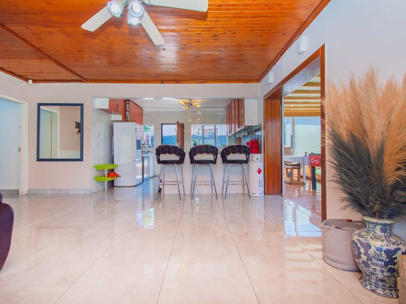 Open plan living area featuring a timber ceiling, ceiling fan, and polished porcelain floor tiles, flowing into a kitchen with a breakfast bar.