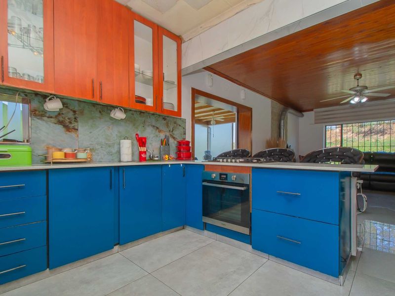 Kitchen featuring vibrant blue and orange cabinetry, stone splashback, built-in oven, gas hob, and tiled flooring, opening into an adjacent living area.