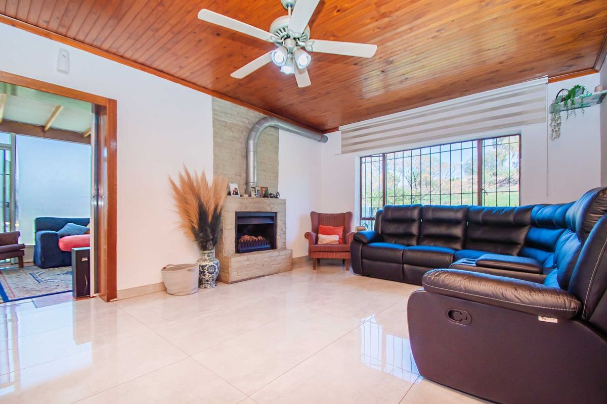 Living room featuring a timber-clad ceiling, tiled flooring, and a stone fireplace with a metal flue, offering a cozy and functional space.