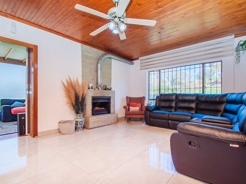 Living room featuring a timber-clad ceiling, tiled flooring, and a stone fireplace with a metal flue, offering a cozy and functional space.