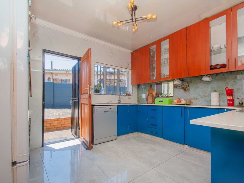 A functional kitchen featuring two-tone cabinetry, stone countertops, tiled flooring, and direct access to the exterior through a security-gated door.