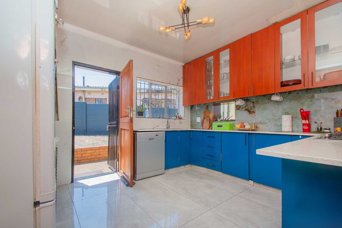 A functional kitchen featuring two-tone cabinetry, stone countertops, tiled flooring, and direct access to the exterior through a security-gated door.