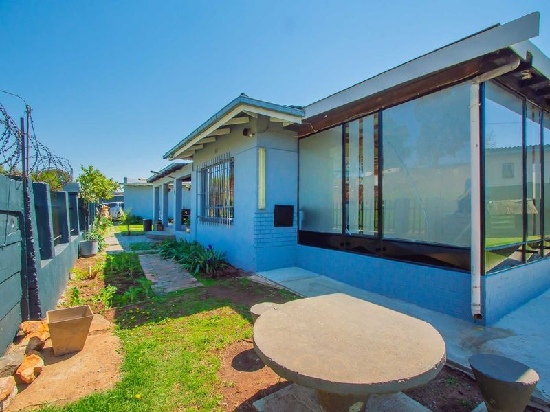 Rear exterior view of the property featuring a paved walkway, concrete boundary wall with security fencing, and a fixed outdoor concrete table.