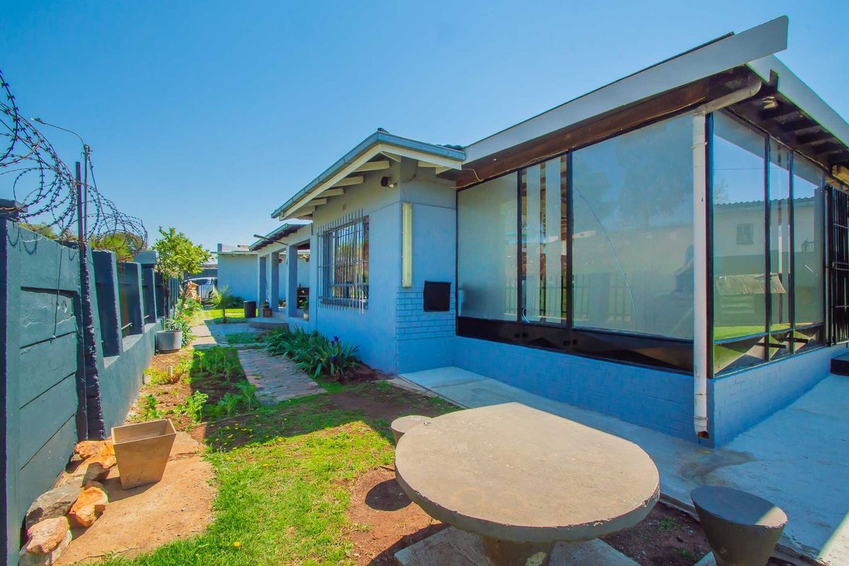 Rear exterior view of the property featuring a paved walkway, concrete boundary wall with security fencing, and a fixed outdoor concrete table.