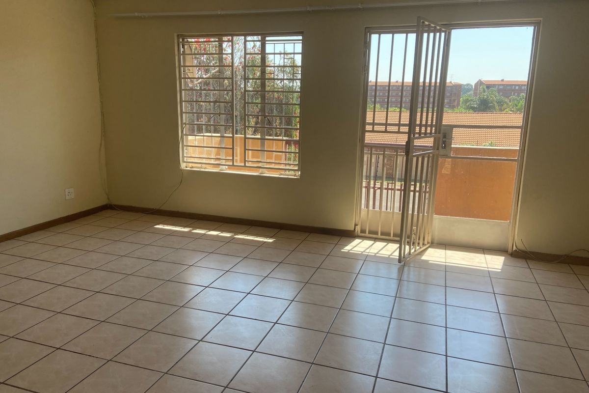 An empty living room featuring tiled flooring, security bars on the windows, and a security gate leading to an outdoor area.