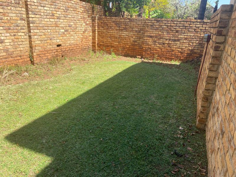 A private backyard area featuring a grass lawn enclosed by high face-brick boundary walls, offering potential for landscaping and outdoor improvement.