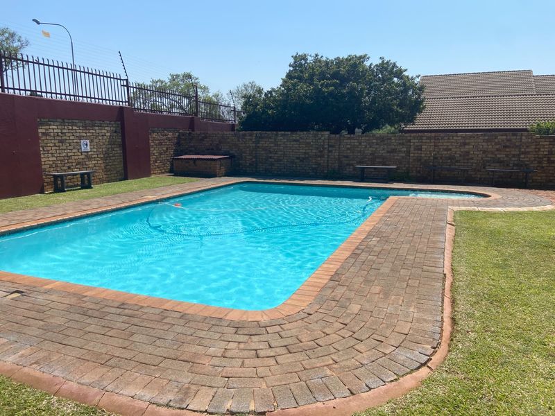 A well-maintained outdoor swimming pool area featuring brick paving, a secure perimeter wall, and electric fencing.