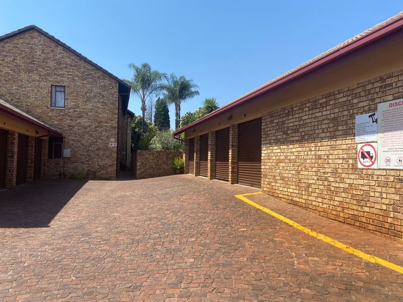 Exterior view of a residential apartment complex featuring a paved driveway and multiple secure roller shutter garage units.