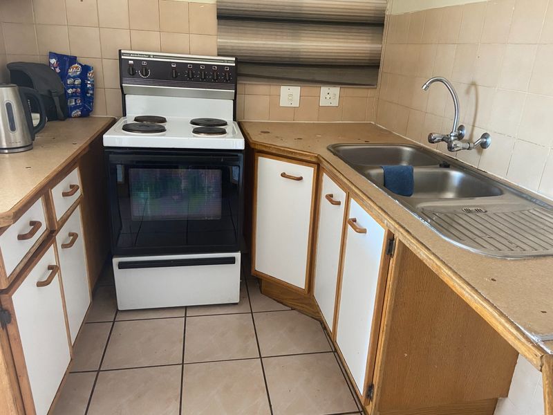 A compact kitchen featuring a freestanding stove, double basin sink, tiled splashback, and dated cabinetry with laminate countertops.
