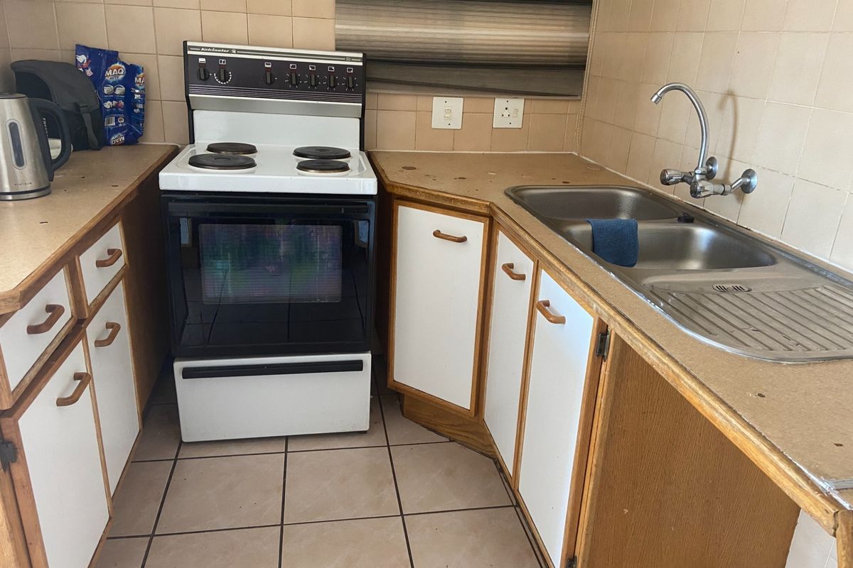 A compact kitchen featuring a freestanding stove, double basin sink, tiled splashback, and dated cabinetry with laminate countertops.