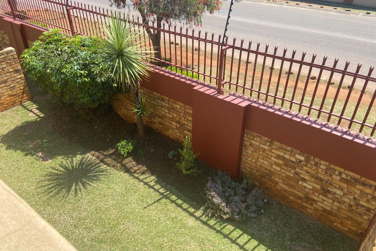 A view of the rear garden area featuring a secure brick boundary wall with integrated steel and electric fencing.