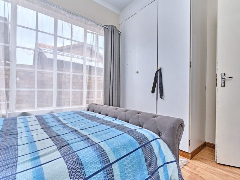 A bedroom featuring laminate flooring, a large window with grid detailing, and built-in cupboards providing storage space.