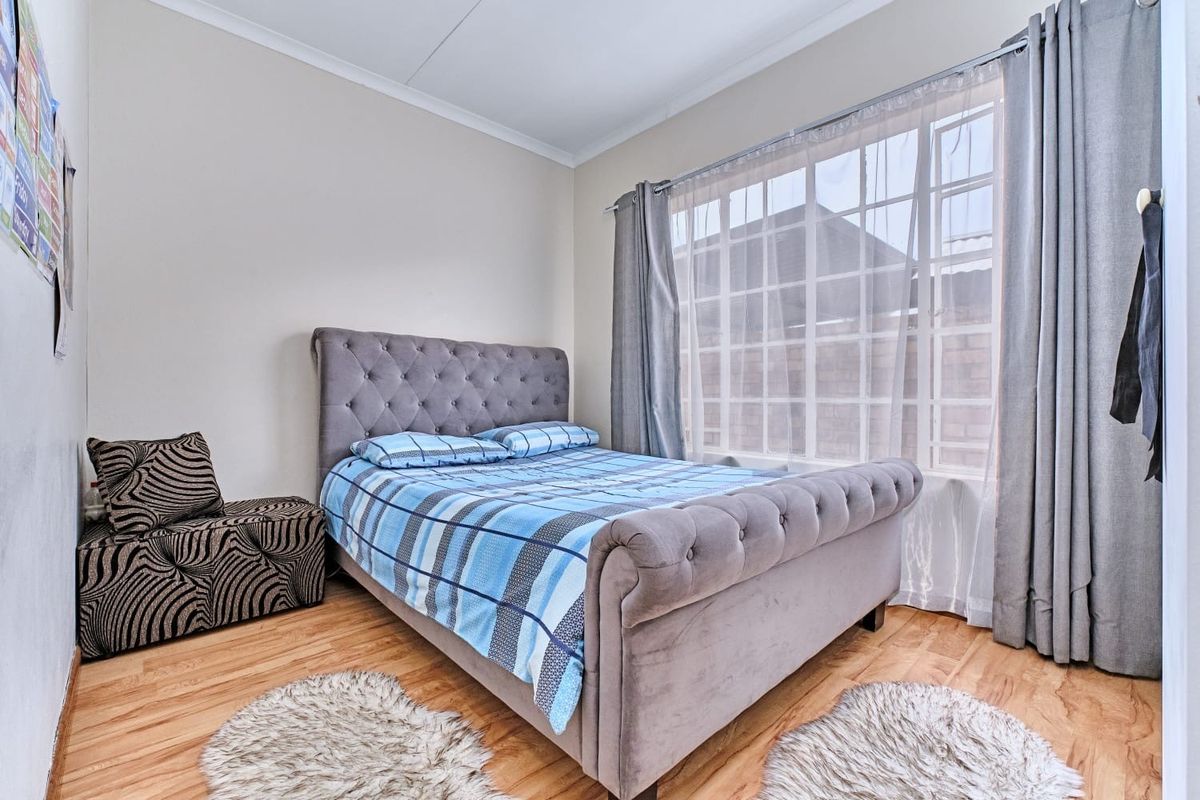A well-lit bedroom featuring laminate flooring and a large grid-pattern window, providing a comfortable and functional living space.