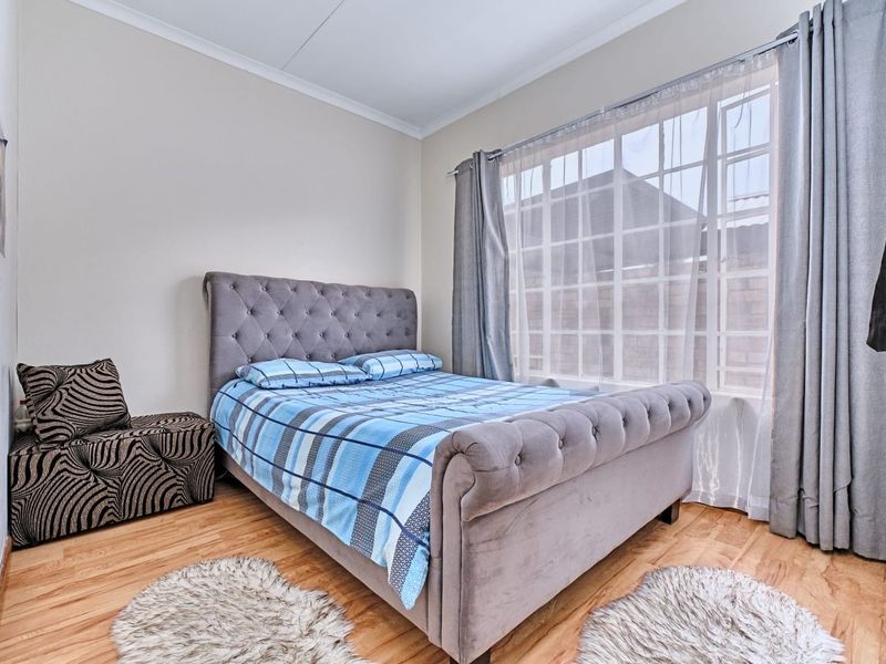 A well-lit bedroom featuring laminate flooring and a large grid-pattern window, providing a comfortable and functional living space.