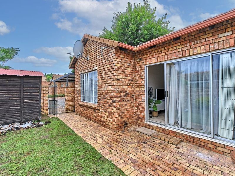 Rear view of a face brick townhouse featuring a paved walkway, sliding door access, and a small garden area with a storage shed.