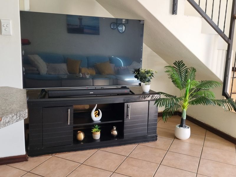 A living area featuring tiled flooring and a staircase with a metal balustrade, situated adjacent to a kitchen counter.