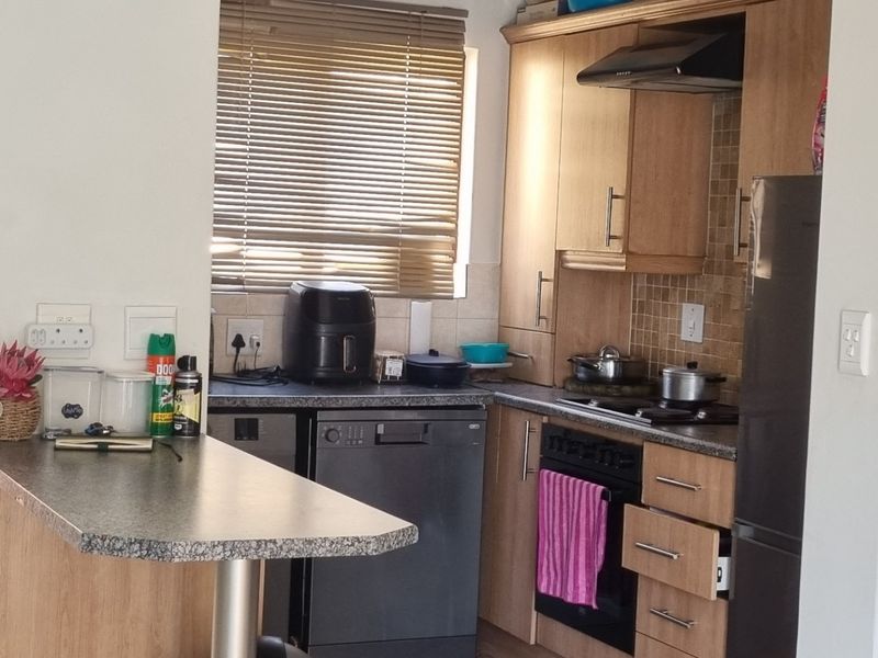Compact kitchen featuring wood-look cabinetry, dark laminate countertops, a tiled backsplash, and integrated appliances including an oven and extractor fan.