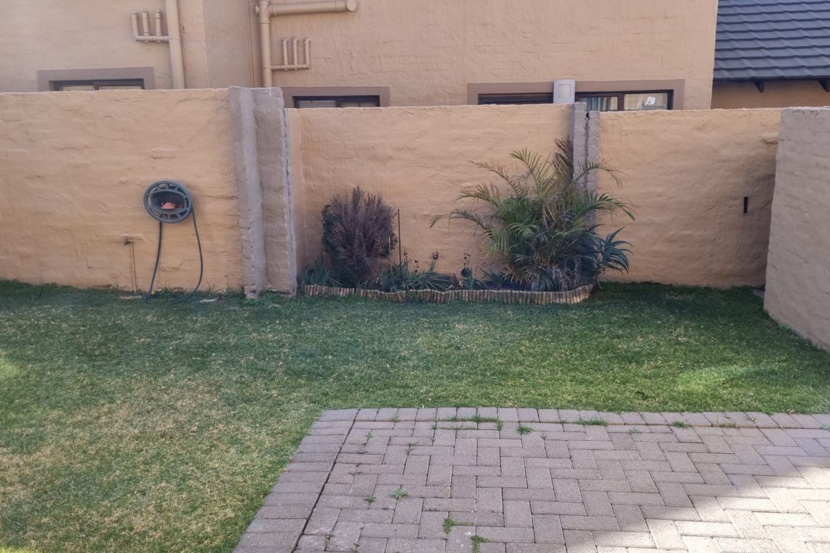 A private rear garden area featuring a paved patio, lawn, and boundary wall with established garden beds.
