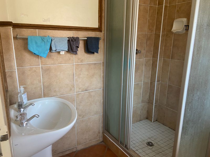 A dated bathroom featuring a pedestal basin, tiled walls, and a shower enclosure with a glass door.