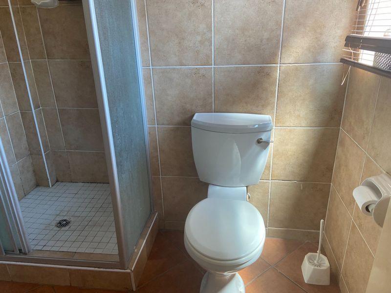 A functional bathroom featuring a shower enclosure, toilet, and neutral ceramic tiling throughout the walls and floor.