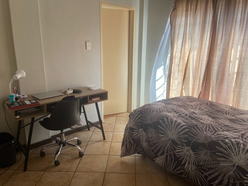 A functional bedroom featuring ceramic floor tiles, neutral wall finishes, and access to a private balcony through sliding glass doors.