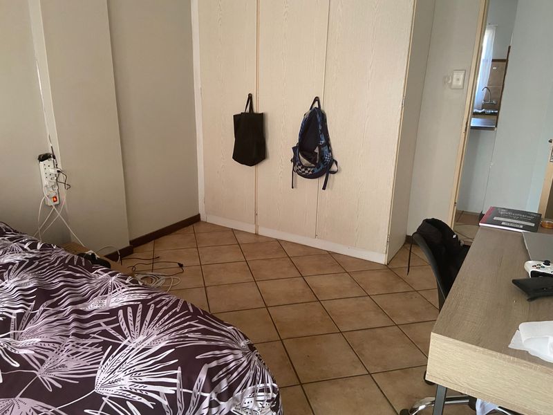 A bedroom featuring tiled flooring and built-in cupboards, with a view into an adjacent kitchen area.