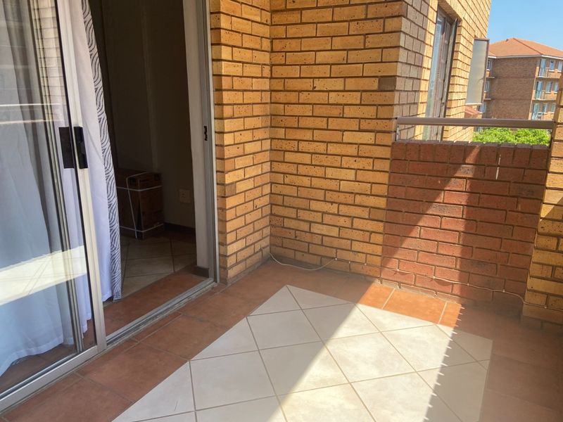 A private balcony featuring brick walls, tiled flooring, and a metal balustrade, accessible via a sliding glass door.