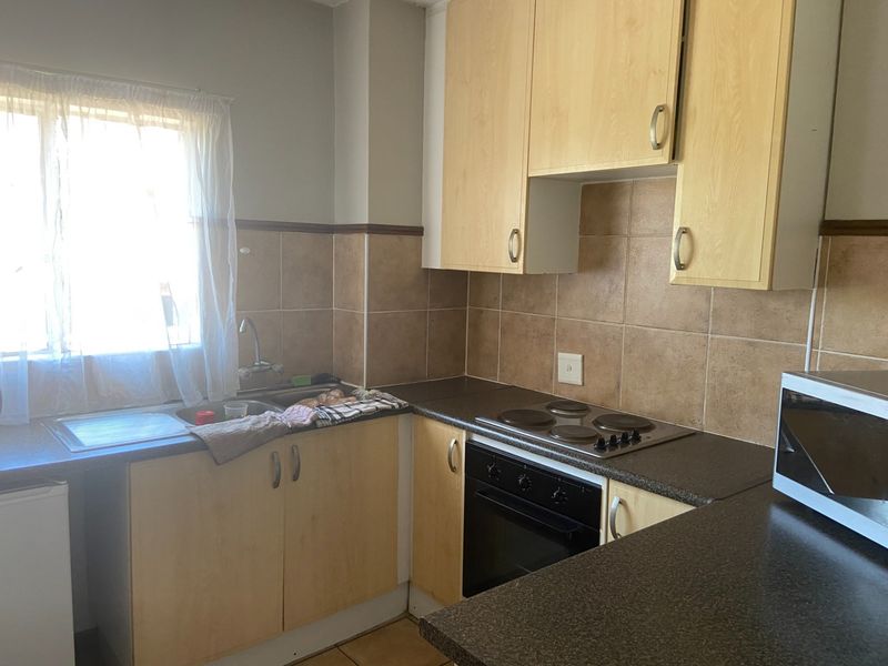 A functional kitchen featuring laminate cabinetry, built-in electric hob and oven, stainless steel sink, and tiled backsplash, offering a practical layout for daily use.