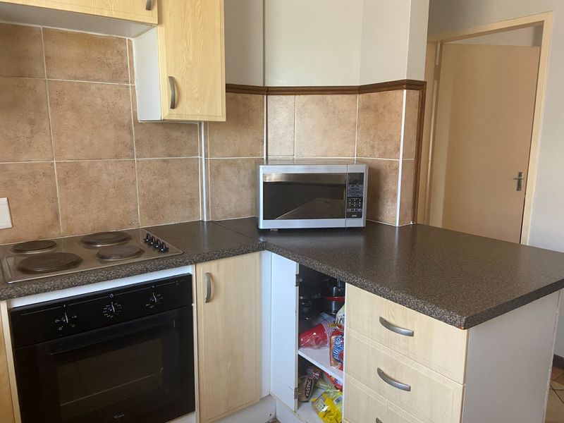 A functional kitchen area featuring built-in cabinetry, an electric oven and hob, and tiled backsplash, requiring minor maintenance to the cabinetry.