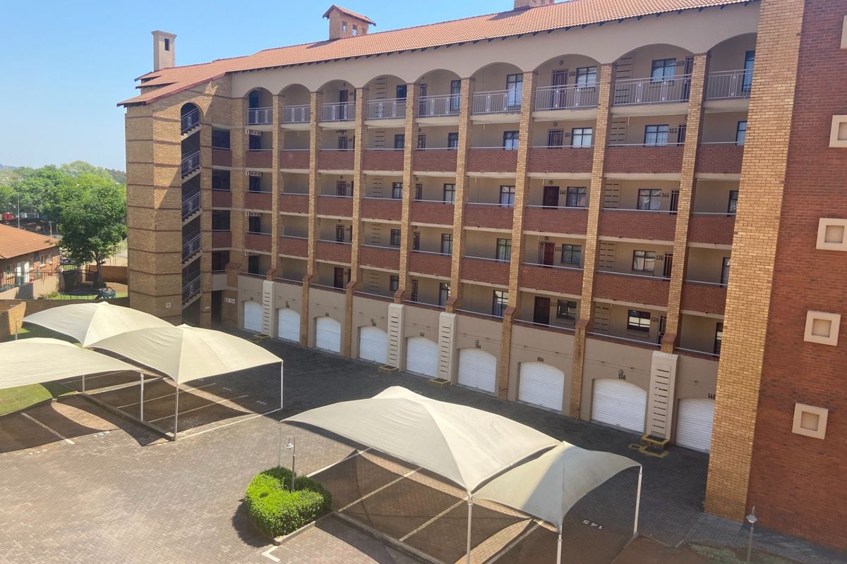 Exterior view of a multi-story apartment complex featuring brick construction, private balconies, ground-level garages, and covered parking bays.