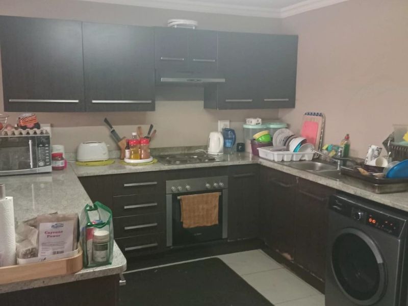 A functional kitchen featuring dark cabinetry, granite countertops, built-in oven, hob, extractor fan, and integrated space for a washing machine.