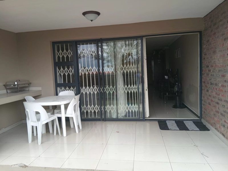 A covered patio area featuring tiled flooring, a built-in counter, and a sliding security gate providing access to the interior living space.
