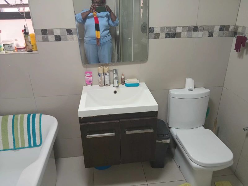 A functional bathroom featuring a wall-mounted vanity with basin, a dual-flush toilet, and a bathtub, finished with neutral ceramic wall and floor tiles.