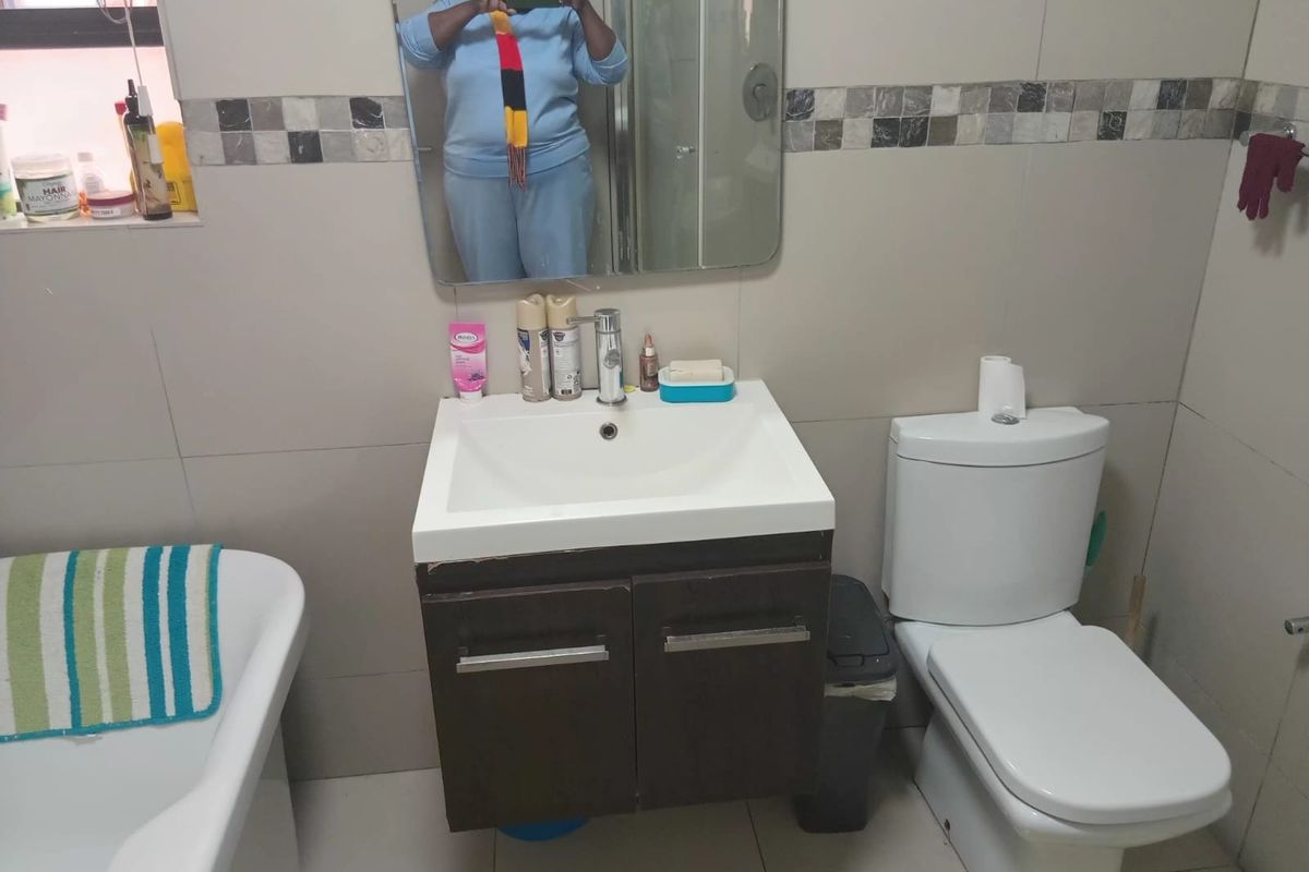 A functional bathroom featuring a wall-mounted vanity with basin, a dual-flush toilet, and a bathtub, finished with neutral ceramic wall and floor tiles.