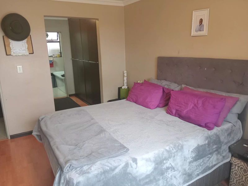 A bedroom featuring laminate flooring, coving, and built-in cupboards, with an adjoining en-suite bathroom visible through the doorway.