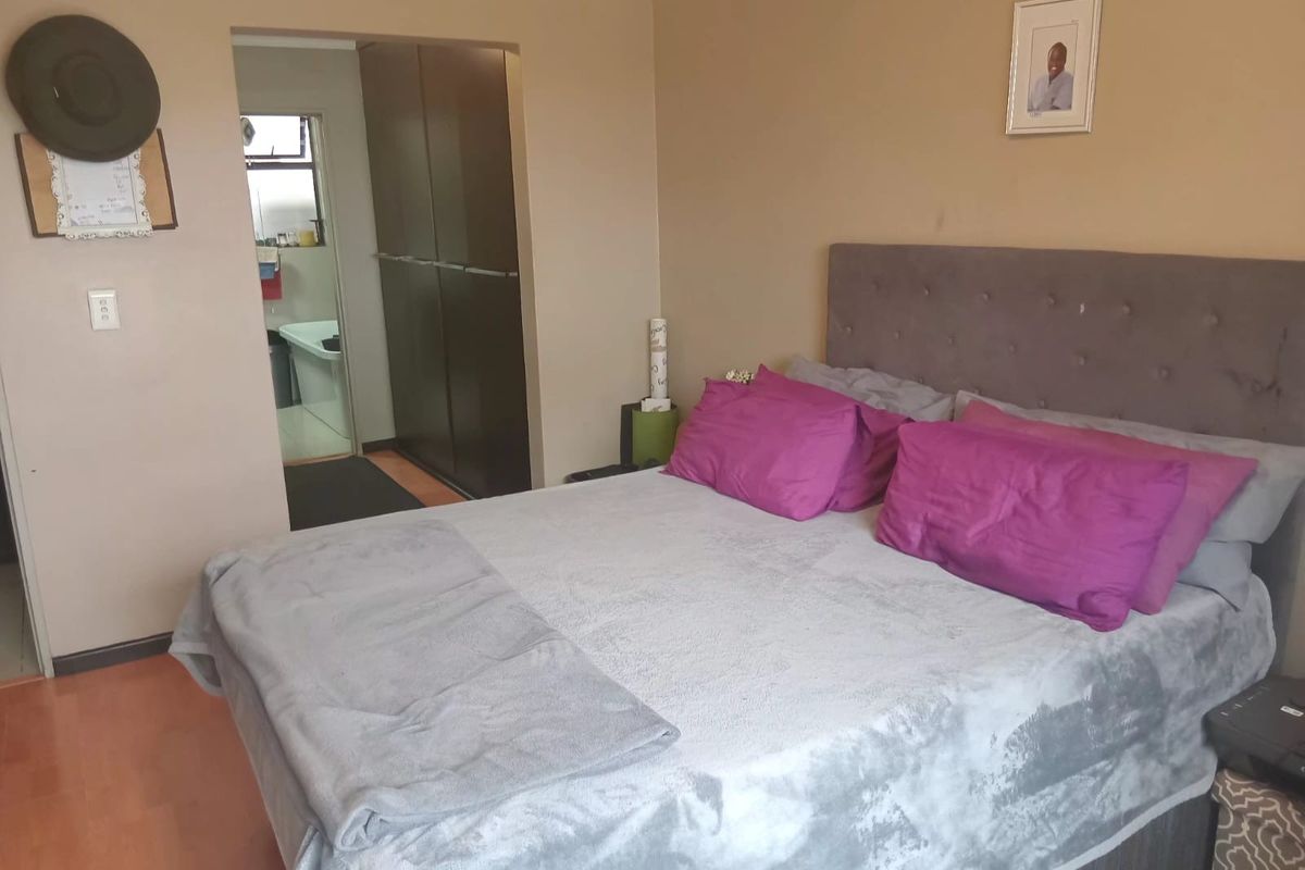 A bedroom featuring laminate flooring, coving, and built-in cupboards, with an adjoining en-suite bathroom visible through the doorway.
