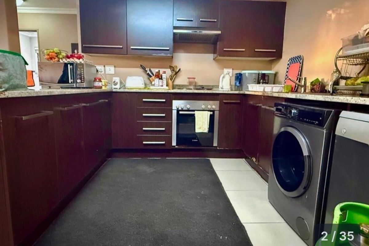 A functional kitchen featuring dark wood cabinetry, granite countertops, a built-in oven, and an integrated extractor fan with tiled flooring.