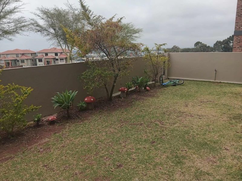 A private garden area featuring a lawn, established shrubs, and a solid boundary wall with an outdoor water tap.