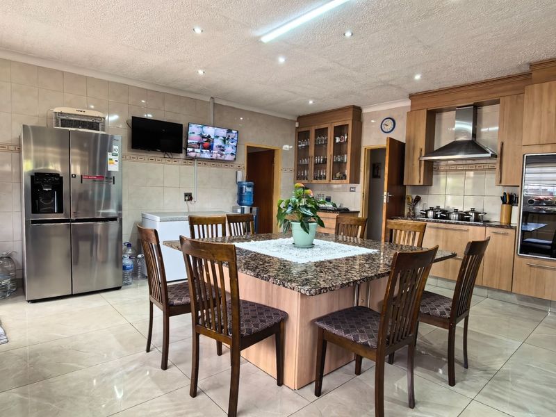 Spacious open-plan kitchen and dining area featuring granite countertops, wooden cabinetry, built-in appliances, and tiled flooring throughout.
