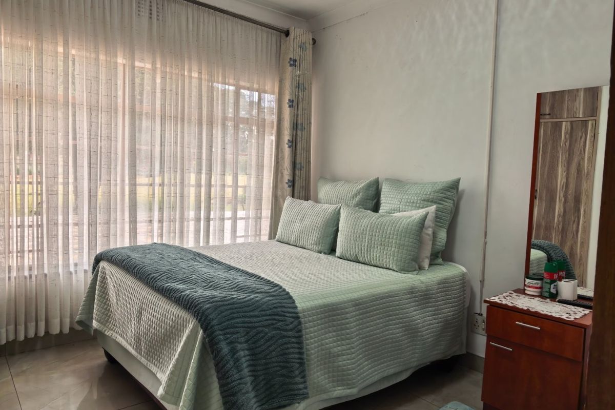 A bedroom featuring tiled flooring, a built-in cupboard, and large windows with curtain rails, offering a functional and comfortable living space.