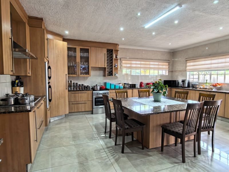 Spacious kitchen featuring extensive wooden cabinetry, granite countertops, integrated appliances, and a central island with dining seating, finished with modern tiled flooring.