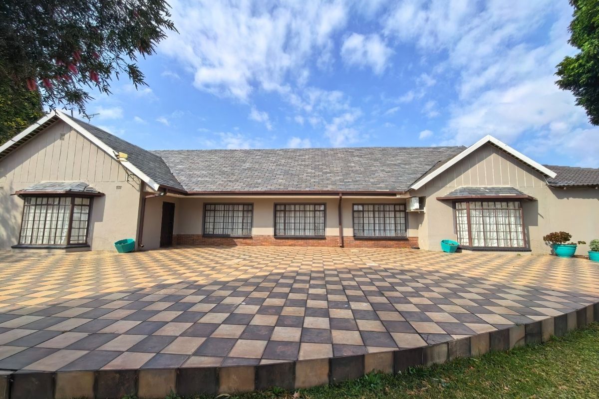 A spacious rear exterior view of the farmhouse featuring a large checkered tiled patio, slate roofing, and multiple bay windows.