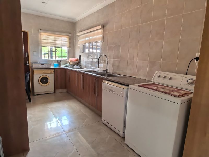A functional laundry room featuring built-in wooden cabinetry, a double stainless steel sink, tiled backsplash, and tiled flooring with natural light from two windows.