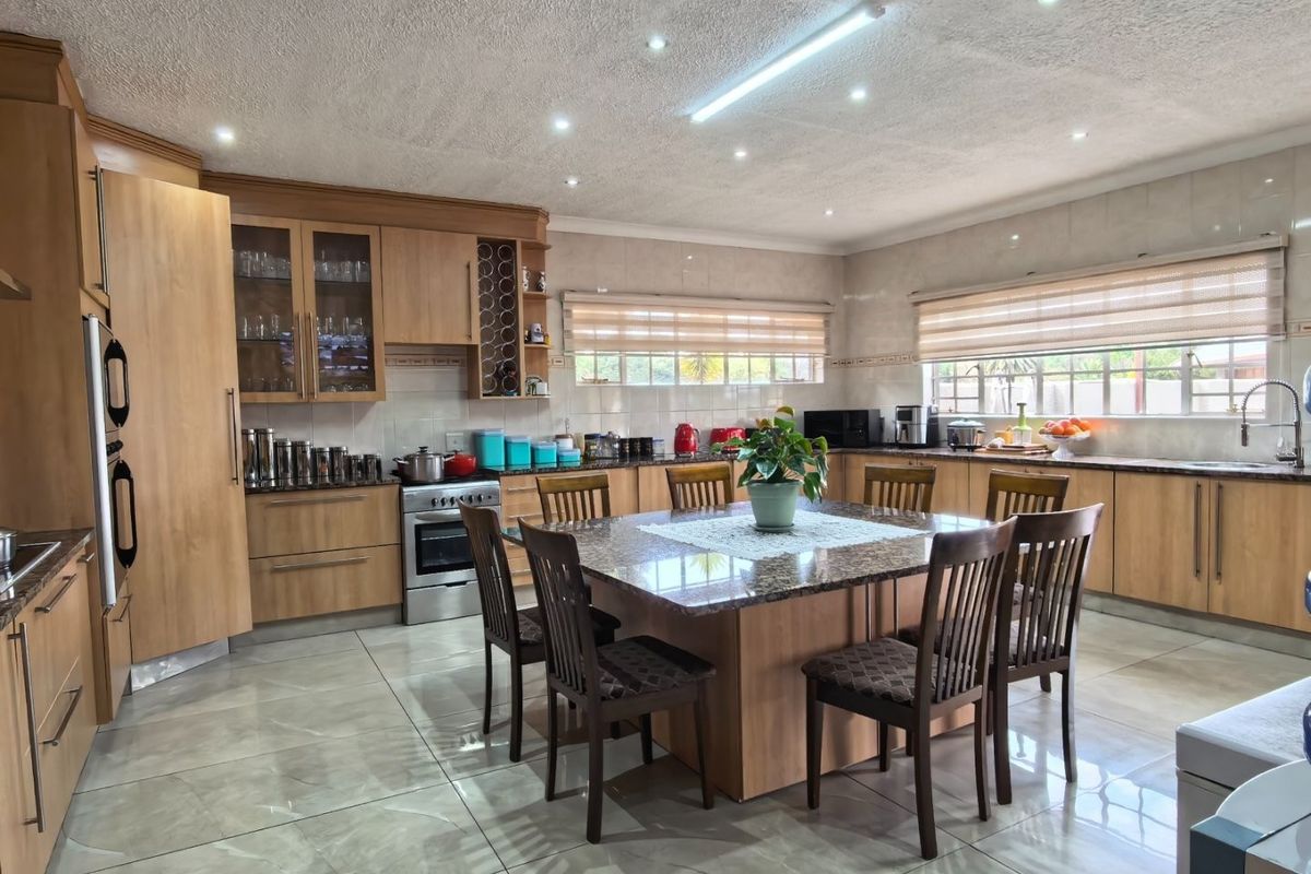 Spacious kitchen featuring light wood cabinetry, granite countertops, a central island, and modern tiled flooring with ample natural light.