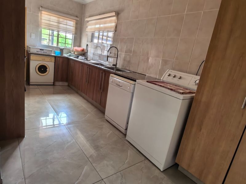 A functional laundry room featuring built-in wooden cabinetry, a double sink, tiled splashbacks, and tiled flooring with space for multiple appliances.